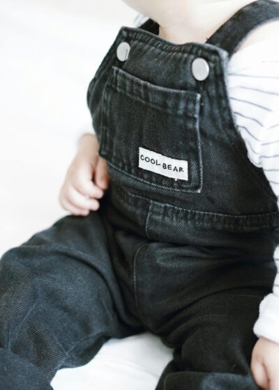 Adorable baby wearing stylish black denim overalls with 'Cool Bear' label.