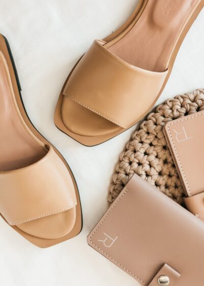 A minimalist flat lay of beige sandals and a matching purse on a textured background.